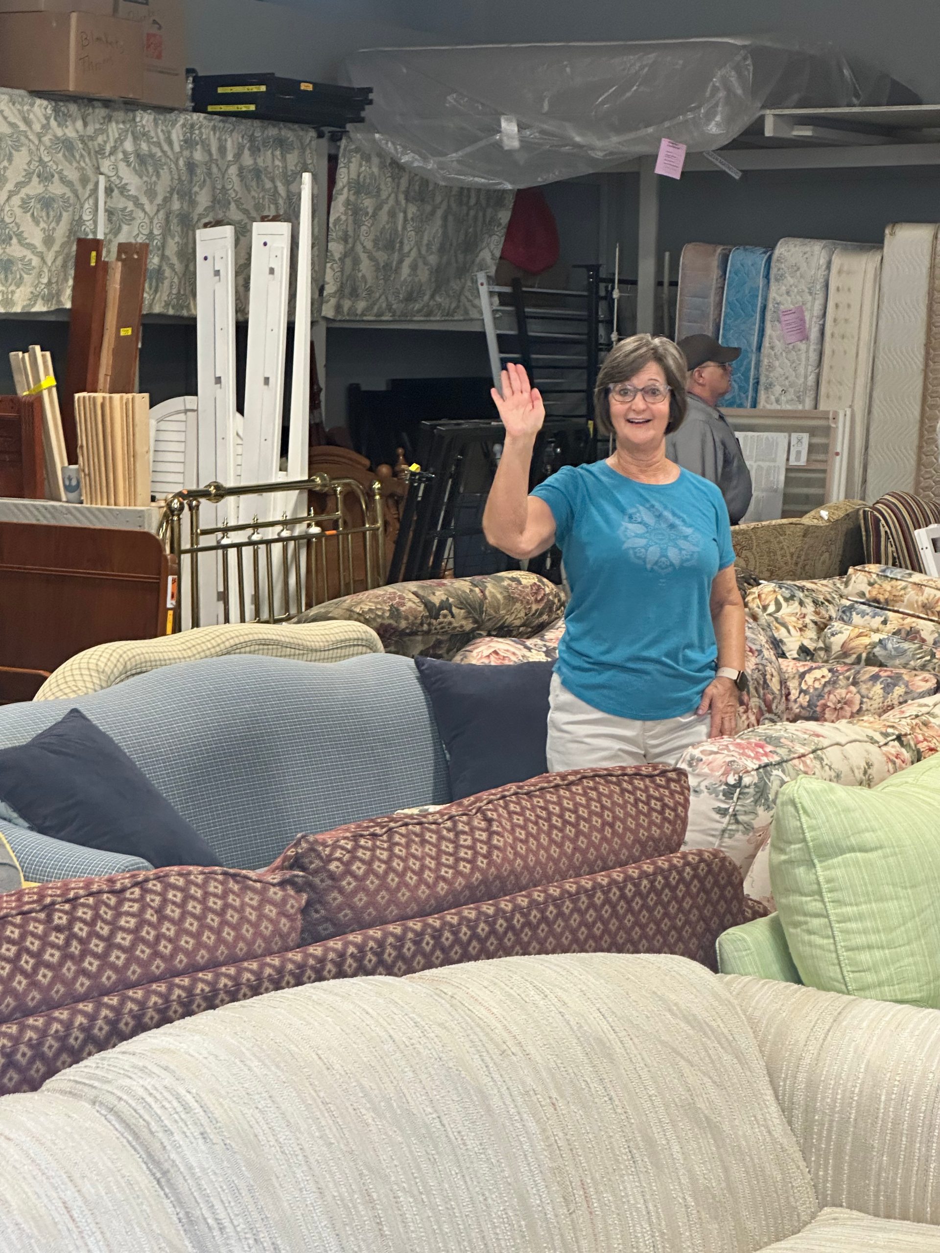 Volunteer waving from among rows of donated couches in The Sharing Shed warehouse