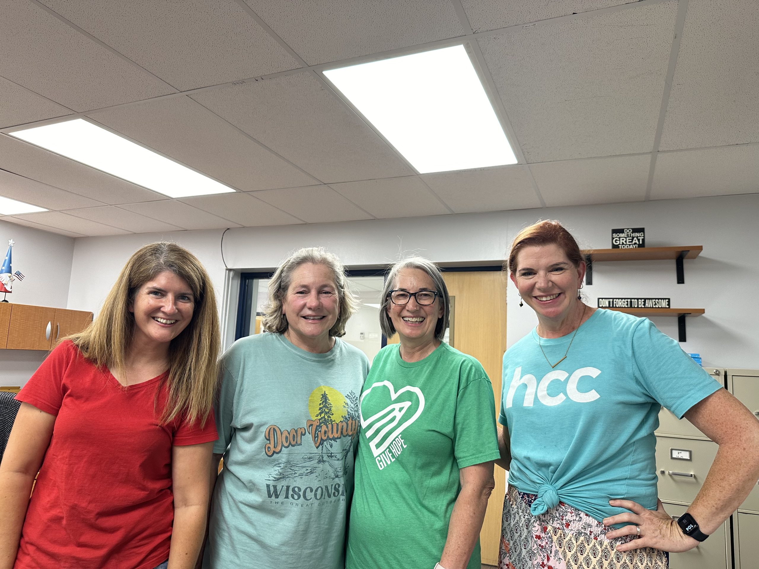 Four smiling small group volunteers, two in HCC shirts, standing together in an office