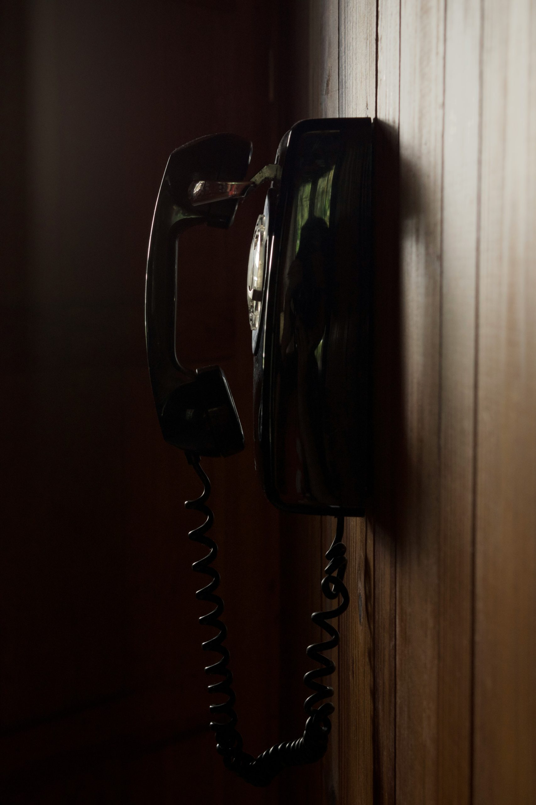 Vintage black rotary phone mounted on a wood-paneled wall