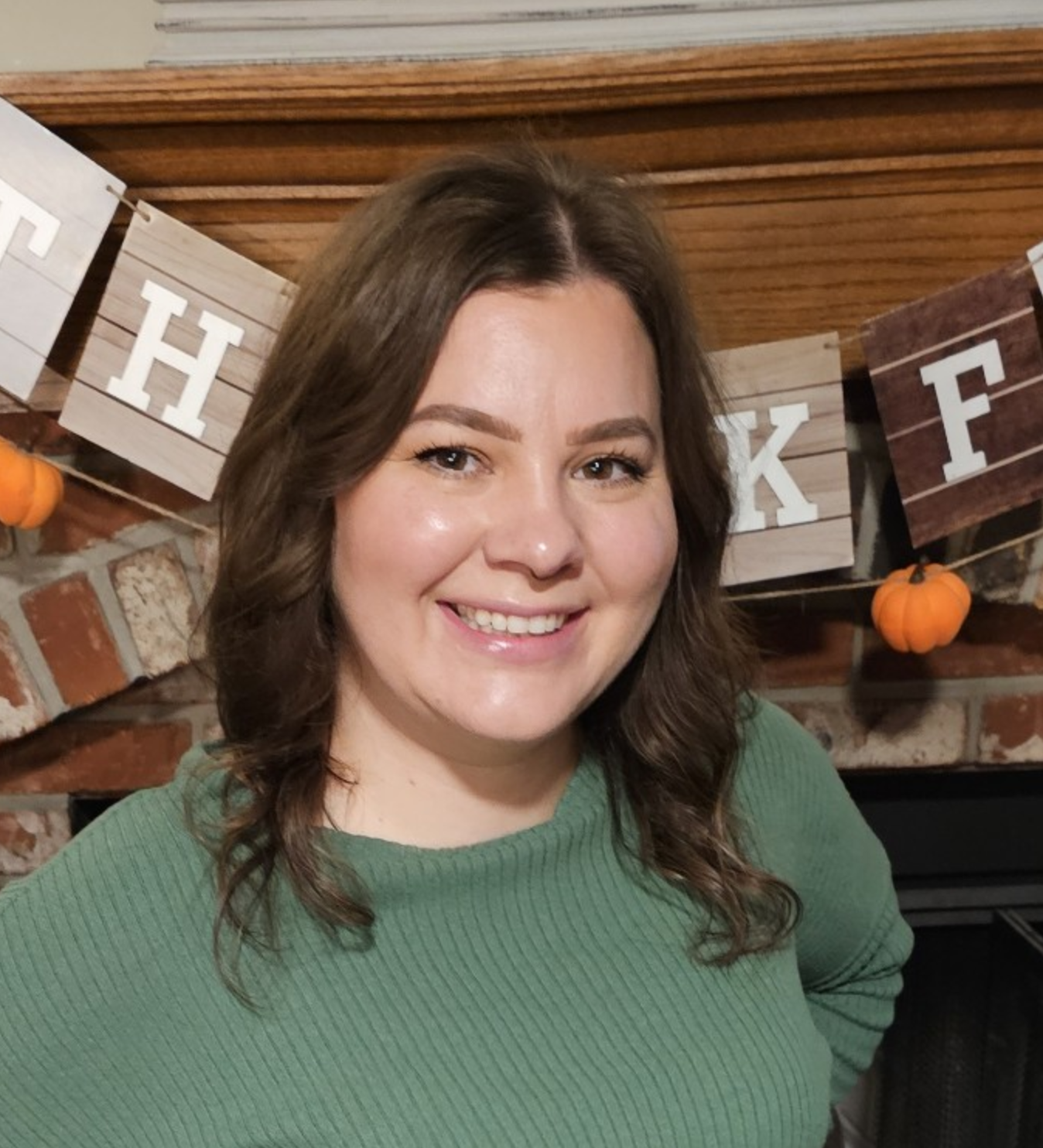 Katy Pursell smiling in front of a fall banner and mantel decorated with pumpkins