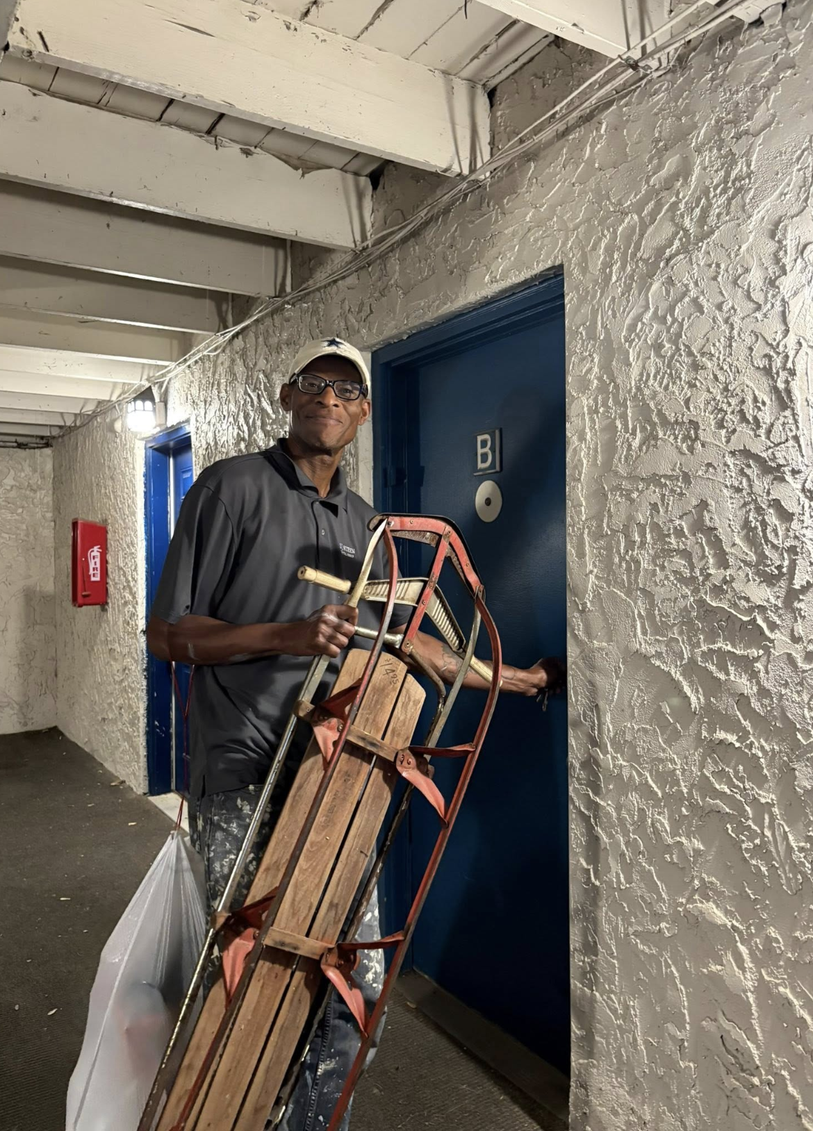 Smiling man at Faith Haven House holding a wooden sled next to an apartment door