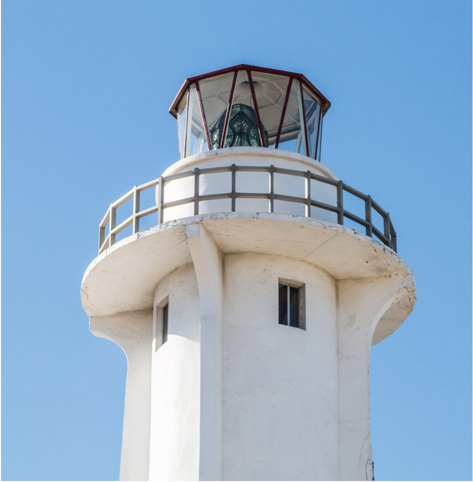 White lighthouse tower with a red-framed lantern room against a clear blue sky