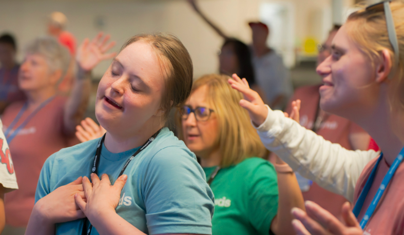 Smiling young woman with Down syndrome worshipping with her eyes closed among other Joni and Friends campers and volunteers