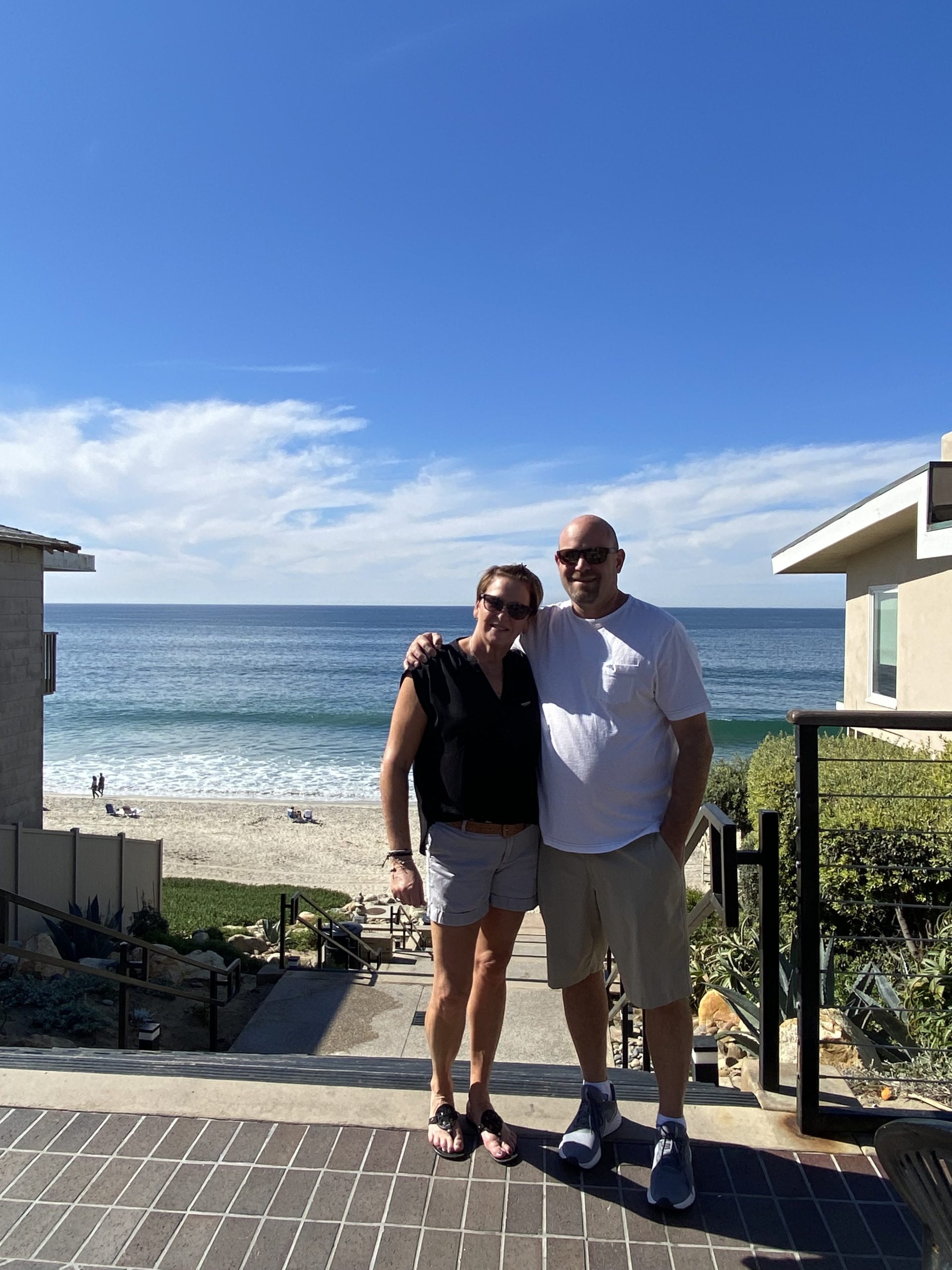 Shannon Sebastian and her husband smiling on a terrace above a sunny beach