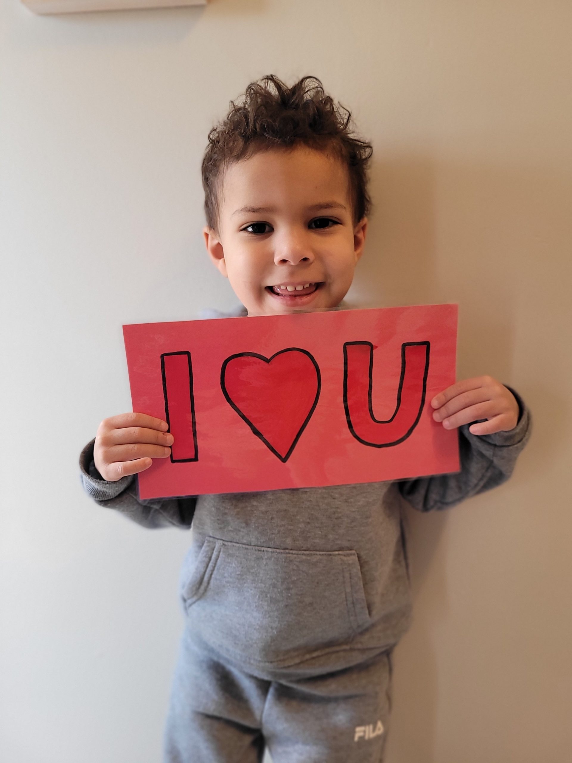 Smiling young boy holding a handmade red 'I heart U' sign