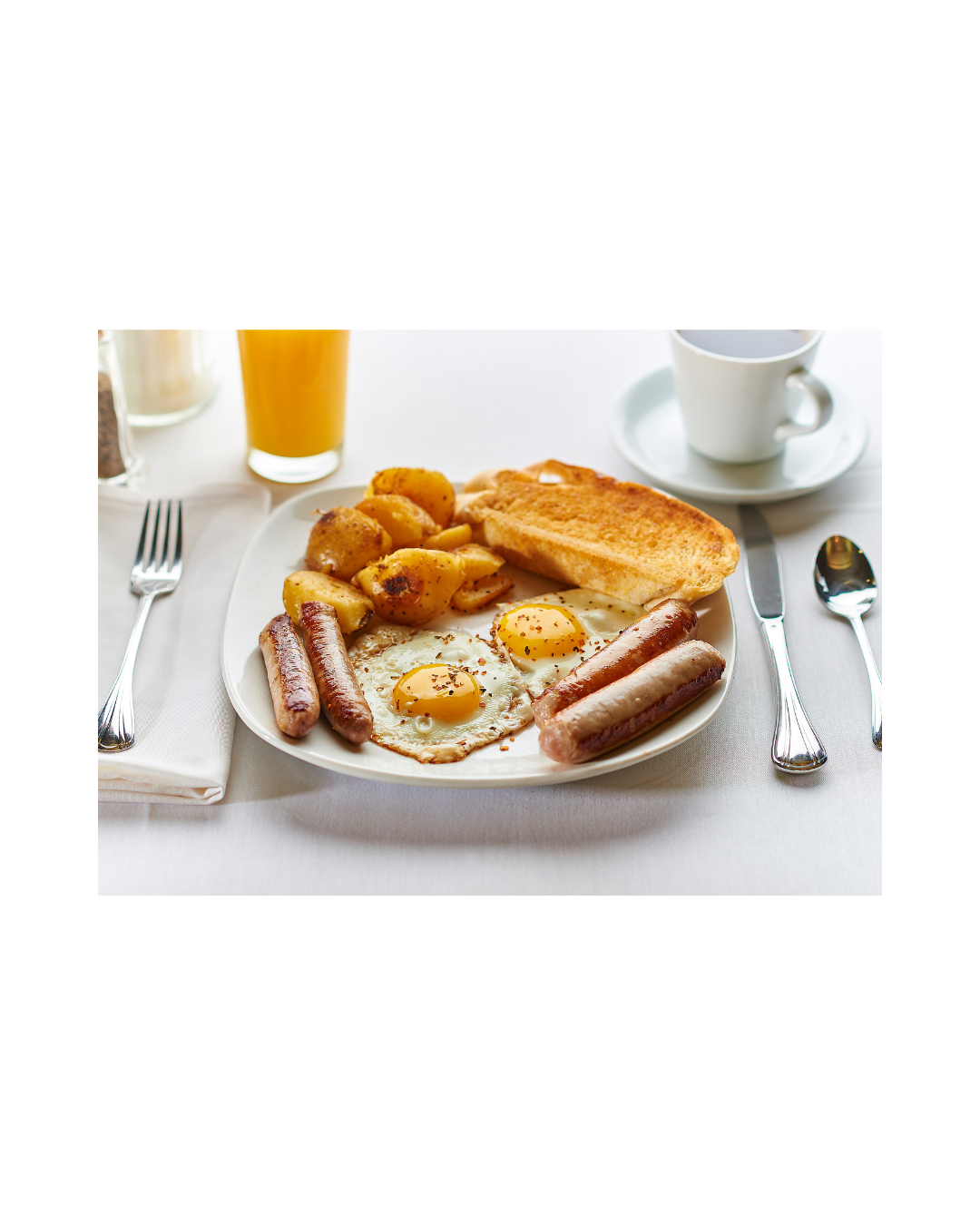 Breakfast plate with fried eggs, sausage links, roasted potatoes and toast, with orange juice and coffee