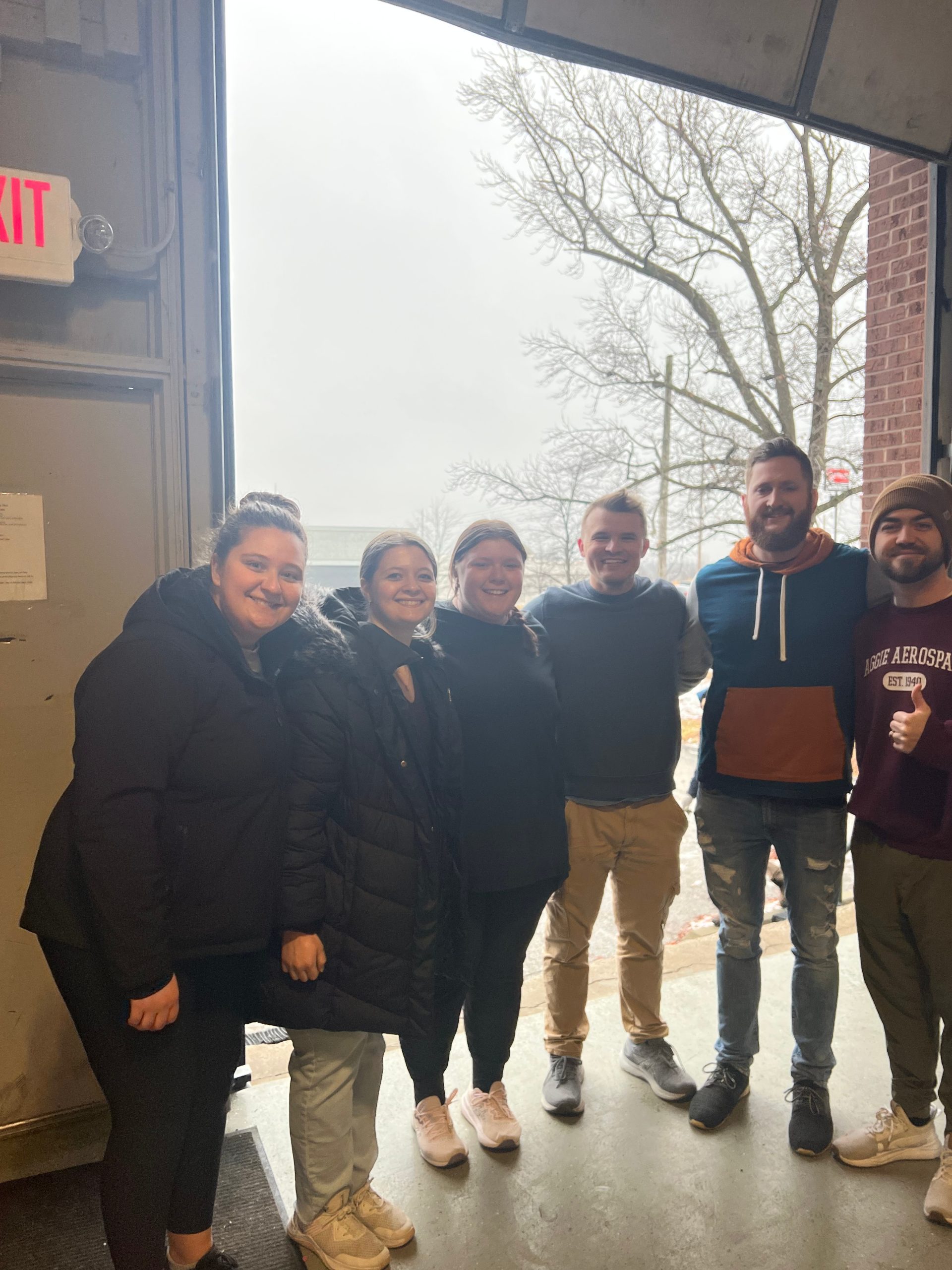 Young adult volunteers smiling together at the open loading door of The Sharing Shed warehouse
