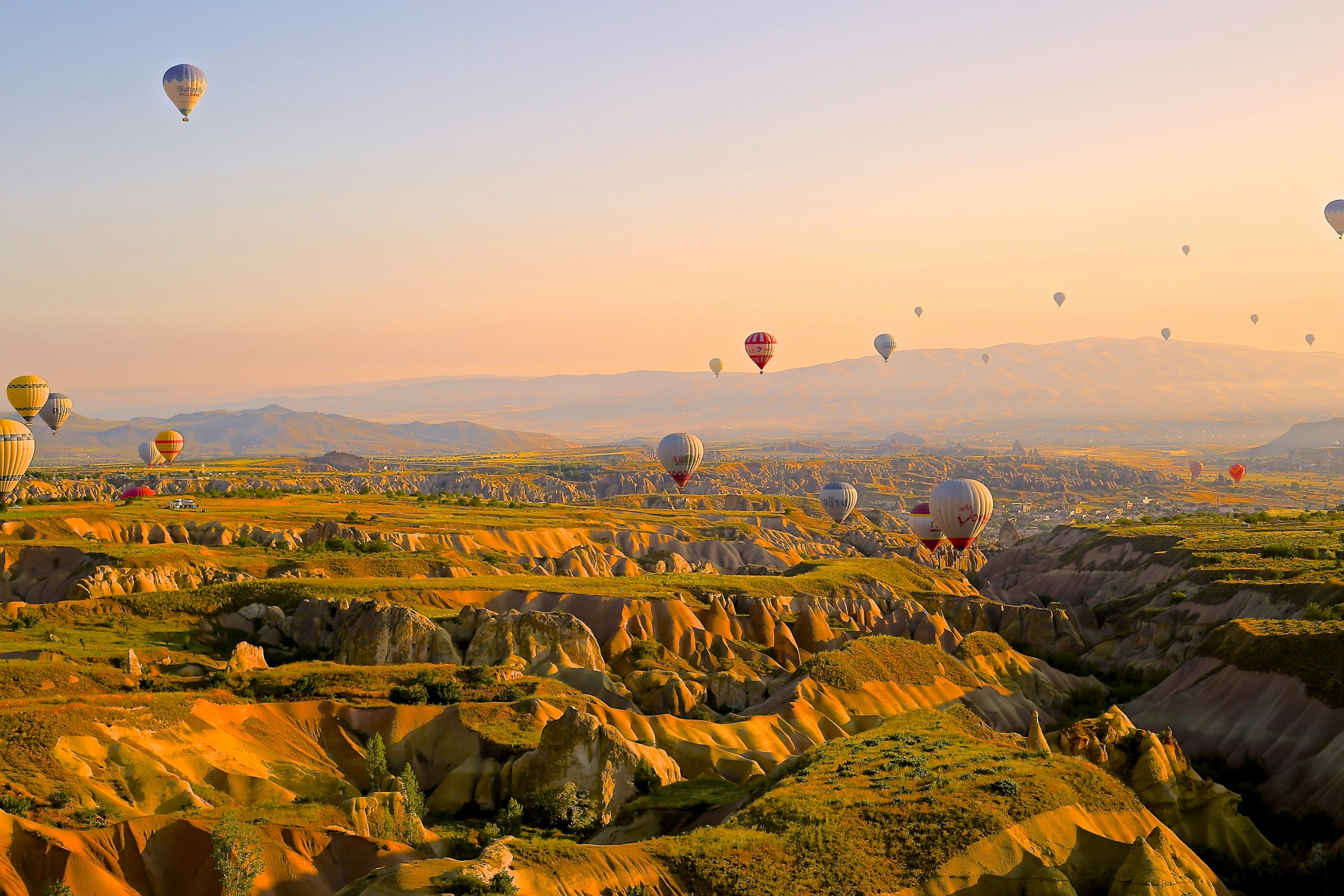 Hot air balloons floating over rugged valleys and hills at sunrise