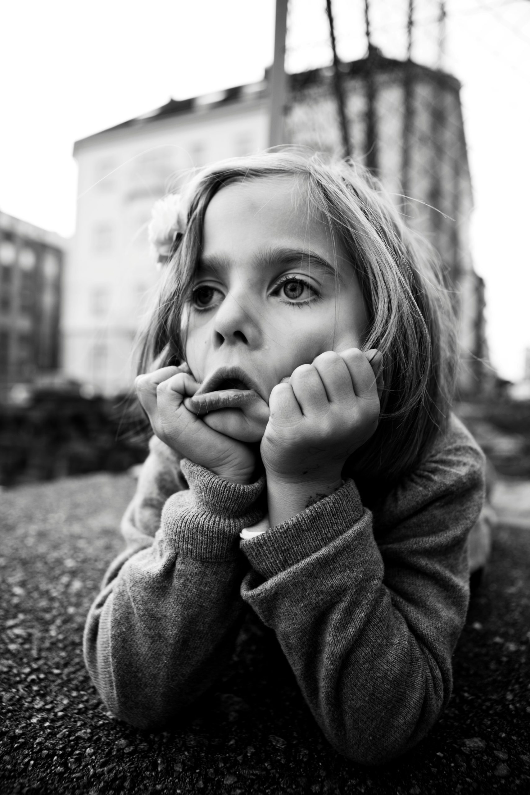 Black and white photo of a young girl lying on the ground with her chin in her hands, looking tired
