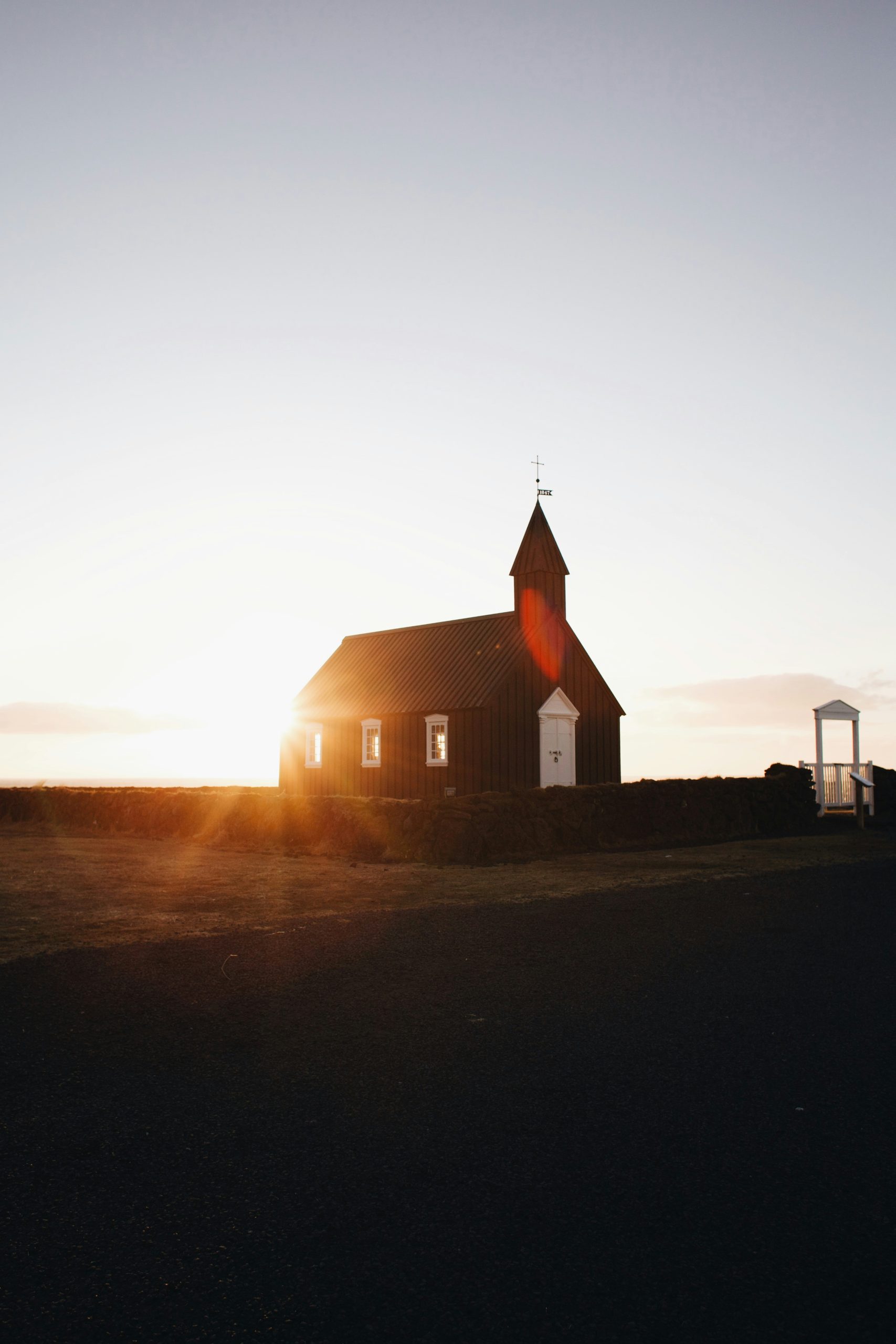 A small dark wooden church with a steeple backlit by the setting sun