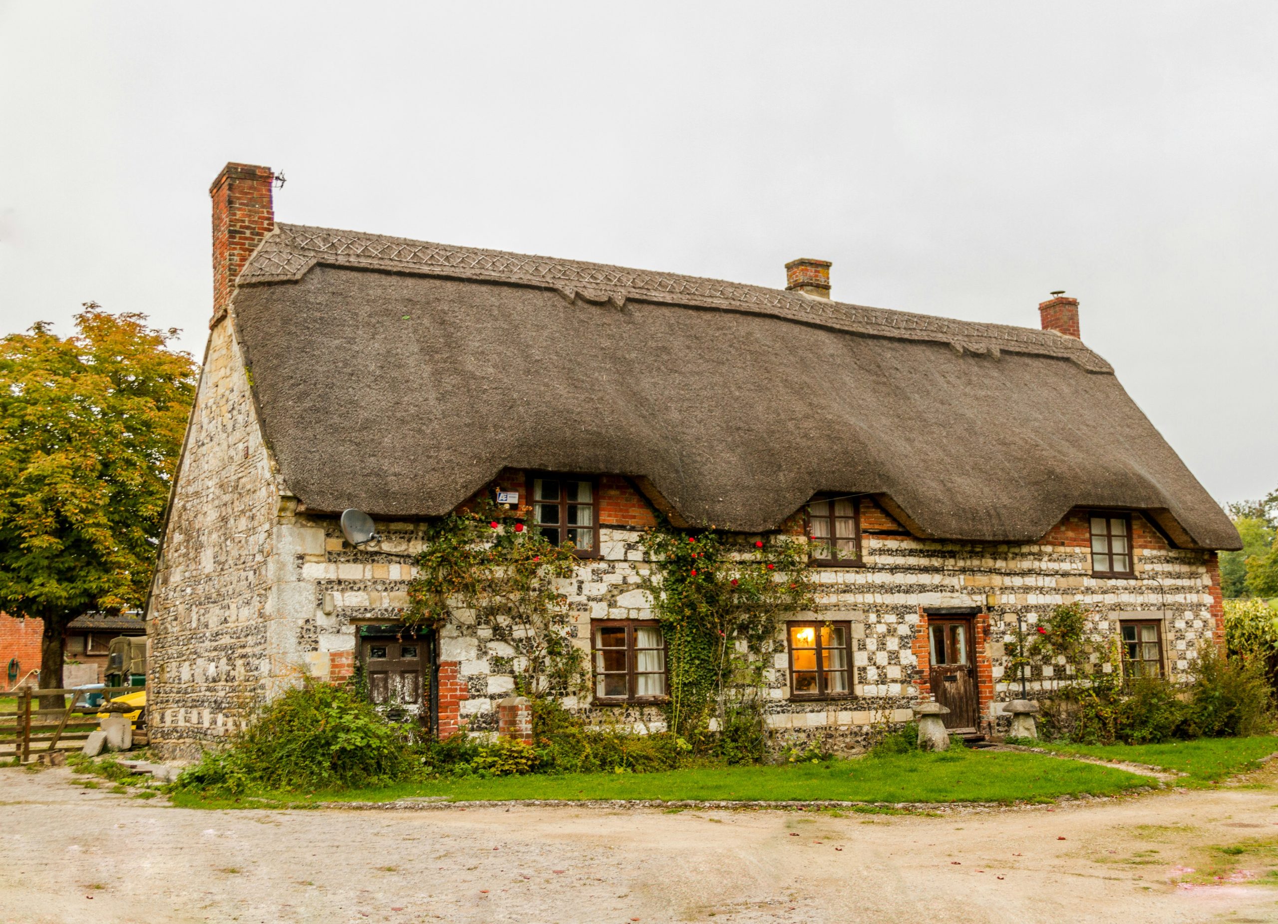 Thatched-roof stone cottage with climbing roses and a lit window
