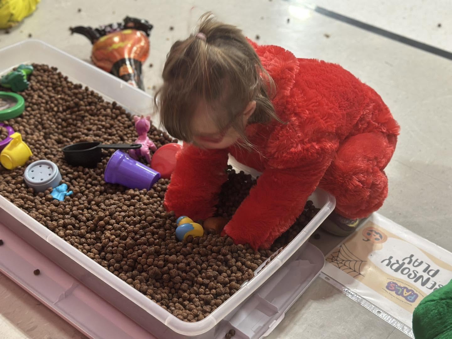 Toddler in a red costume playing in a sensory bin at a Parents As Teachers event