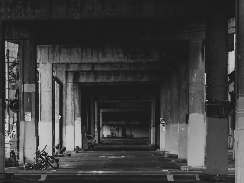 Black and white view down an empty concrete underpass with a bicycle lying by a pillar